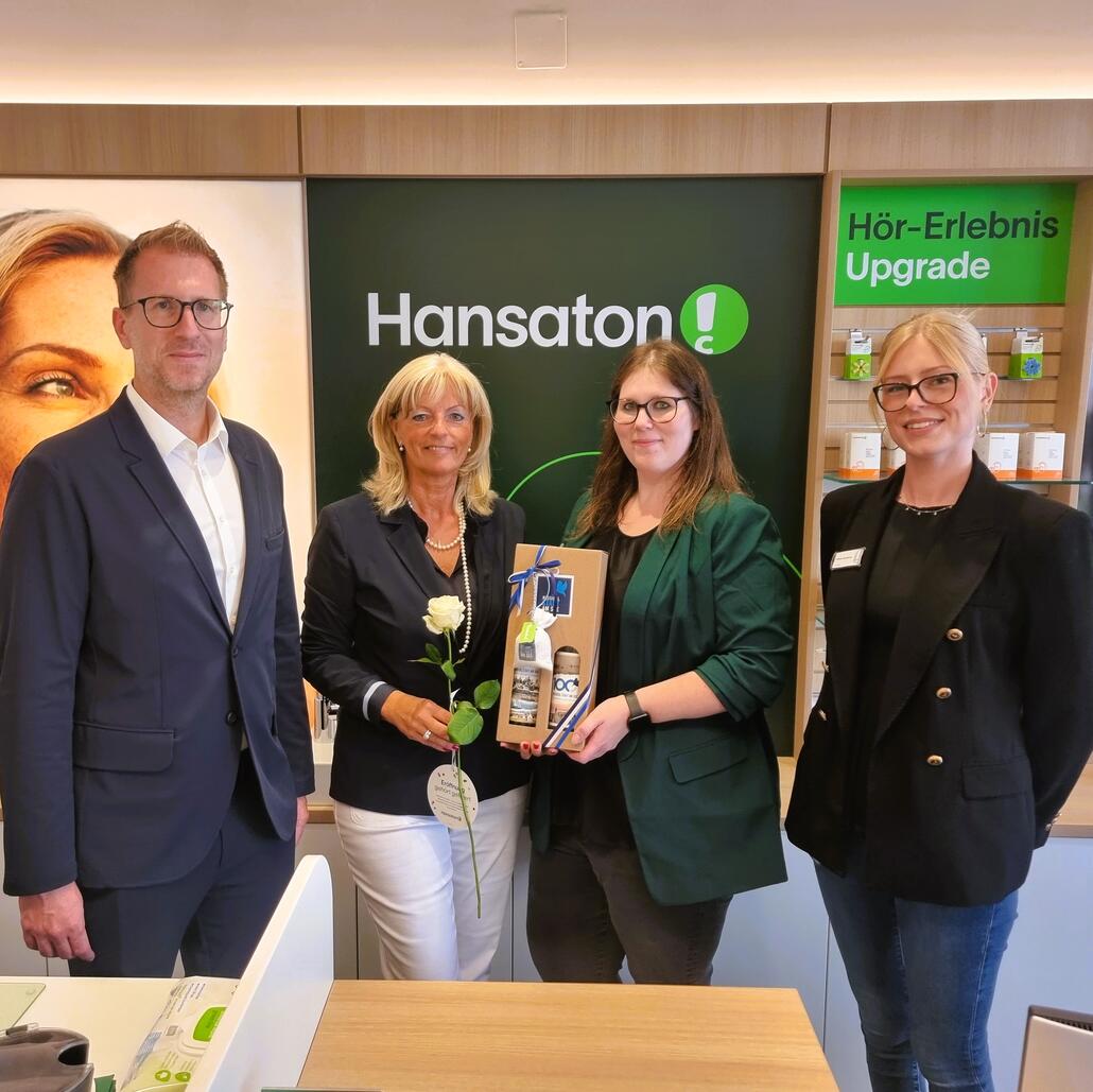 Hansaton-Mitarbeiterinnen und Mitarbeiter mit Geschenk und Rose in einem Geschäft