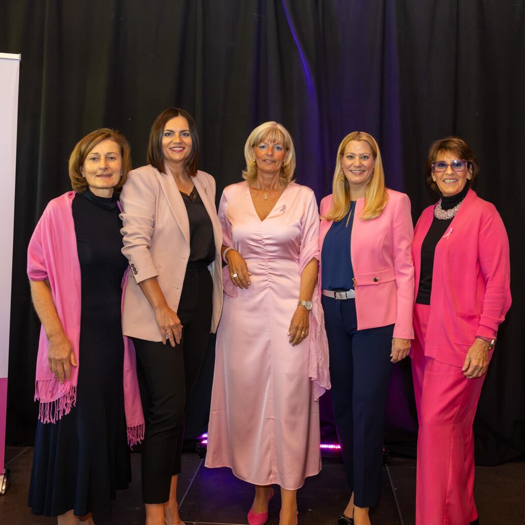 Fünf Frauen in rosa Kleidung stehen nebeneinander vor schwarzem Hintergrund
