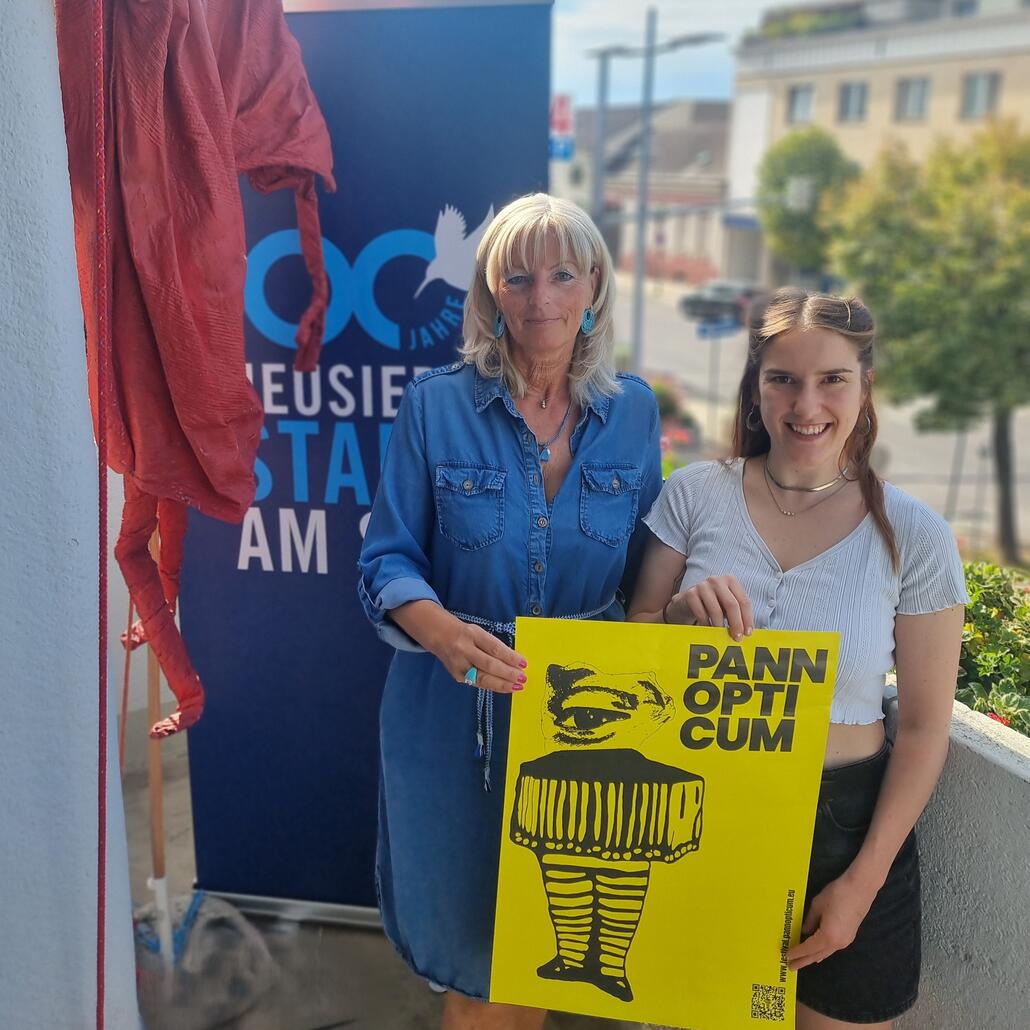 Susanne K. und Lisa M. halten ein gelbes Plakat mit der Aufschrift „Pann Opticum“ in der Hand.