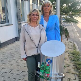 Bürgermeisterin LAbg. Elisabeth Böhm und Umwelt-Gemeinderätin Gerda Kappel zeigen den Pfandring auf einem Mülleimer im Stadtzentrum.